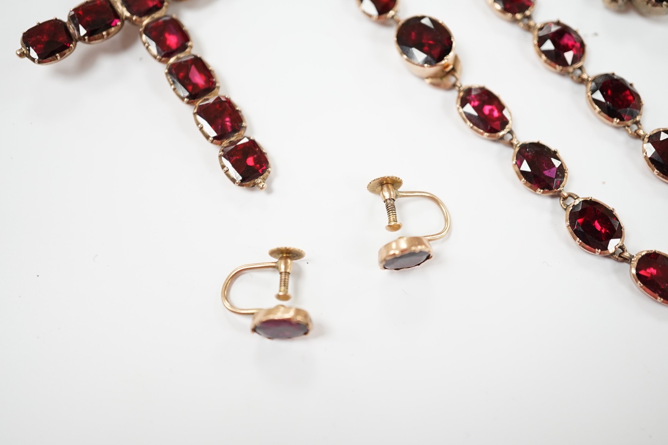 Six items of Victorian oval cut garnet set jewellery, including a yellow metal necklace (lacking drops?), 37cm, a pair of 9ct ear clips, a yellow metal cross pendant with cushion cut stones, gross weight 30 grams and a p